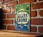 A vintage-style sign for Sierra Leone is displayed on a brick wall.