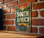 A vintage metal sign with the text "SOUTH AFRICA" displayed on a brick wall.