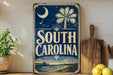 a vintage-style sign that reads "SOUTH CAROLINA" with a palm tree and a crescent moon design. The sign is displayed on a shelf next to a wooden cutting board and a potted plant.