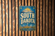A vintage metal sign with the text "SOUTH DAKOTA" and a sun graphic, mounted on a wooden wall.
