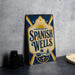 A vintage-style metal sign with the text "Spanish Wells" displayed prominently, featuring a sun and palm tree design.