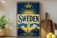 A vintage-style metal sign with the word "SWEDEN" prominently displayed, featuring a sunburst design and a depiction of a Swedish landscape. The sign is placed on a shelf next to a wooden cutting board and a potted plant.