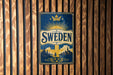 A vintage metal sign with the word "SWEDEN" prominently displayed, featuring a sunburst design and a castle in the background.