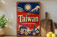 A vintage-style metal sign with the word "Taiwan" prominently displayed, featuring a sun, mountains, and traditional Chinese architecture. The sign is placed on a shelf next to a wooden cutting board and some potted plants.