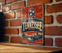 A vintage-style metal sign with the word "TENNESSEE" prominently displayed, featuring a red and blue design with a star and a mountain backdrop.