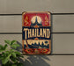 A vintage-style metal sign with the word "Thailand" prominently displayed, featuring a temple and other traditional Thai imagery.