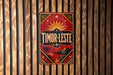 A vintage-style metal sign with a red background and gold accents, featuring a sun and palm trees, is hanging on a wooden wall.