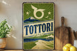 a vintage-style sign with a mountain landscape and a bird, placed on a wooden surface next to a wooden cutting board and some lemons.