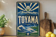 A vintage-style sign for Toyama, featuring a mountain landscape and a wave, is displayed on a shelf next to a wooden cutting board and some lemons.
