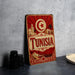 A vintage-style metal sign with the word "TUNISIA" prominently displayed, featuring a crescent moon and star symbol, along with an illustration of a desert landscape and buildings.