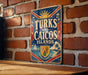 A vintage-style sign displaying the name "TURKS AND CAICOS ISLANDS" against a brick wall background.