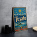 A vintage-style metal sign with the word "Tuvalu" on it, featuring a tropical island and sun design, is displayed on a gray countertop next to some black camera lenses.