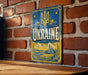 A vintage metal sign with the word "UKRAINE" prominently displayed, featuring a castle and other architectural elements, mounted on a brick wall.