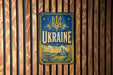 A vintage-style metal sign with the word "UKRAINE" prominently displayed, featuring a blue background with a yellow border and decorative elements.