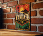 A vintage metal sign with the word "VANUATU" prominently displayed, featuring a tropical landscape with palm trees and a sun.