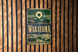 A vintage metal sign with the text "Wakayama" displayed prominently, mounted on a wooden wall.