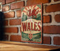 A vintage metal sign with a red dragon and the word "Wales" displayed on a brick wall.