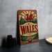A vintage metal sign with a red dragon and the word "Wales" on it, placed on a gray countertop next to some black camera lenses.