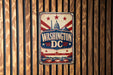 A vintage-style metal sign with the text "WASHINGTON DC" prominently displayed, featuring a stylized depiction of the United States Capitol building and stars.