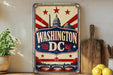A vintage-style metal sign with the text "WASHINGTON DC" prominently displayed, featuring a stylized depiction of the Washington Monument and other iconic landmarks. The sign is placed on a wooden surface, with a potted plant, a cutting board, and some lemons nearby.