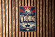 A vintage-style metal sign with the word "Wyoming" prominently displayed, featuring a cowboy silhouette and a mountain landscape.