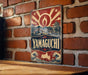 A vintage-style metal sign with a red and blue design hangs on a brick wall, featuring the word "YAMAGUCHI" prominently displayed.