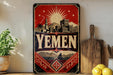 a vintage-style metal sign with the word "Yemen" prominently displayed, surrounded by a decorative border and a sunburst design. The sign is placed on a shelf next to a wooden cutting board and a potted plant, creating a homely and rustic atmosphere.