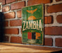 a vintage-style sign with the word "Zambia" prominently displayed, mounted on a brick wall.