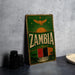 a vintage Zambia beer sign with a green background and gold accents, placed on a gray countertop next to a stack of black camera lenses.
