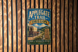 A vintage metal sign for the Applegate Trail in Oregon, featuring a wagon train and a scenic mountain landscape.