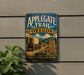 A vintage-style metal sign for the Applegate Trail in Oregon, featuring a wagon train and a scenic landscape.