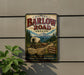 a vintage-style metal sign with a wagon on a trail, surrounded by a forest and mountains, advertising the historic Barlow Road in Oregon.