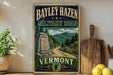 A vintage metal sign for the Bayley Hazen Military Road in Vermont, featuring a scenic mountain landscape and a road leading through the forest.