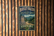 A vintage metal sign for the Bayley Hazen Military Road in Vermont, featuring a scenic mountain landscape and a road leading through the forest.