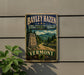 A vintage metal sign for Bayley Hazen Military Road in Vermont, featuring a scenic mountain landscape and a road leading through the forest.
