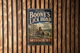 A vintage metal sign advertising "Boone's Lick Road" in Missouri, featuring a wagon and a sign with directions to various locations.