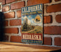 A vintage-style metal sign for the California National Historic Trail in Nebraska, featuring an illustration of a covered wagon and the text "Follow the Trail of History".