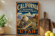 A vintage-style metal sign with the text "California National Historic Trail - Utah" and an illustration of a wagon on a trail in a desert landscape with mountains in the background.