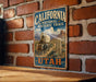 A vintage-style metal sign with the text "CALIFORNIA NATIONAL HISTORIC TRAIL - UTAH" and an illustration of a wagon on a trail, mounted on a brick wall.