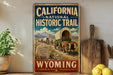 A vintage-style metal sign for the California National Historic Trail, featuring an illustration of a wagon train traveling through a scenic landscape with mountains in the background.