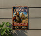 A metal sign featuring a portrait of a bearded man, with the text "CAPTAIN JOHN SMITH" and "CHESAPPEAK" prominently displayed. The sign is mounted on a gray wall, with a plant visible to the left.