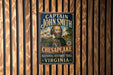 A vintage-style metal sign with the text "CAPTAIN JOHN SMITH" and "CHESAPEKE NATIONAL HISTORIC TRAIL VIRGINIA" is displayed on a wooden wall.
