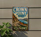 A vintage metal sign for the Crown Point Road in Vermont, featuring a scenic road winding through a mountainous landscape with a lake in the background.