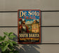 A vintage metal sign advertising the De Soto Trail in South Dakota, featuring a knight in armor and a mountain landscape.