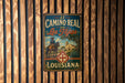 A vintage metal sign with the text "El Camino Real de los Tejas Louisiana" hanging on a wooden wall.