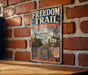 A vintage metal sign for the Freedom Trail in Massachusetts, featuring an illustration of a historic building and a statue, mounted on a brick wall.