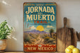 A vintage-style metal sign for the Jornada del Muerto Trail in New Mexico, featuring a desert landscape with mountains and a sun in the background.