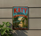 A vintage-style metal sign for the Katy Trail in Missouri, featuring a scenic illustration of a path surrounded by nature.