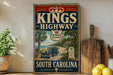 A vintage-style sign for Kings Highway in South Carolina, featuring a car driving on a road surrounded by palm trees and a beach.
