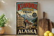 A vintage-style poster advertising Klondike Gold Rush Trail in Alaska, featuring a mountain landscape and a person hiking.